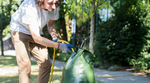 A person fills a tree watering bag up from the hose