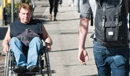 Man in wheelchair rolling on the sidewalk down Commercial Drive